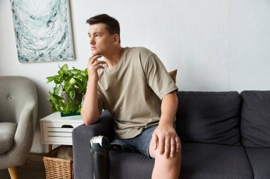 Yakışıklı genç adam kanepede oturur, derin düşüncelere dalmış, protez bacağını şık bir yerde sergiliyor..