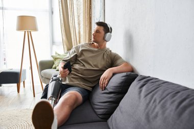 Protez bacaklı genç adam rahat bir kanepede uzanırken müziği sever..