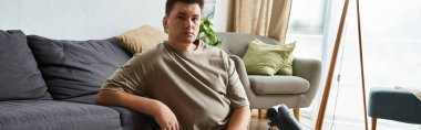 Genç bir adam evindeki parlak bir odada kanepede dinleniyor..