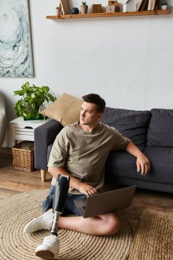 Yakışıklı genç adam yerde dizüstü bilgisayarla oturup, rahatlamış bir yerde protez bacağını gösteriyor..
