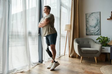 Protez bacaklı yakışıklı genç adam evindeki pencereden dikkatlice dışarı bakıyor..