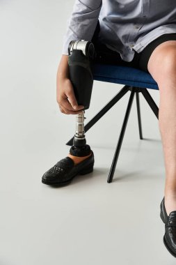 Young man adjusts his stylish prosthetic leg while sitting casually on a chair clipart