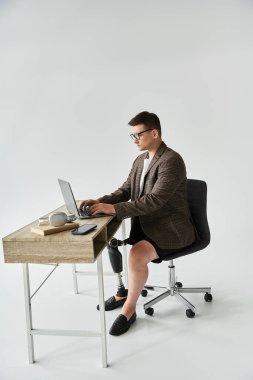 Man sits at a desk typing on a laptop, showcasing his prosthetic leg while focused on work. clipart