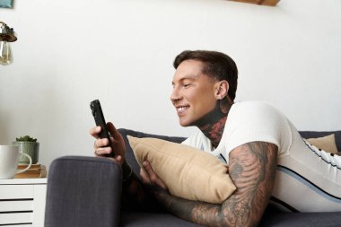 Dövmeli genç adam telefonunu kontrol ederken koltukta dinlenmekten zevk alıyor..