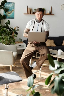 Dövmeleri olan genç bir adam, parlak bir odadaki dizüstü bilgisayarına odaklanmış bir sandalyede oturuyor..