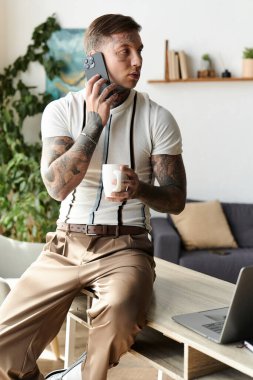 Dövmeleri olan yakışıklı genç adam rastgele oturuyor, elinde kahve tutuyor ve telefonla konuşuyor..
