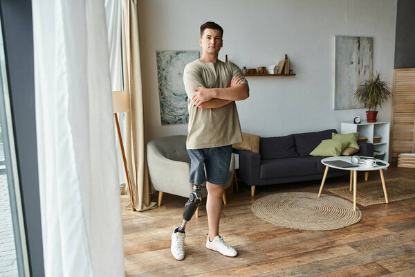 Молодой человек с протезом ноги демонстрирует уверенность, стоя в стильной гостиной.