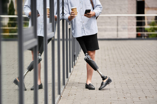 Красивый молодой человек с протезной ногой расслабился, потягивая кофе и пользуясь телефоном на улице..
