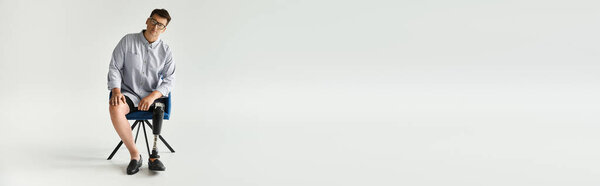Handsome young man with a prosthetic leg sits on a chair in a minimalist studio environment.