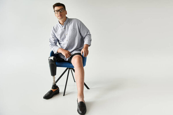 A young handsome man with a prosthetic leg sits in a chair, showcasing his style and confidence.