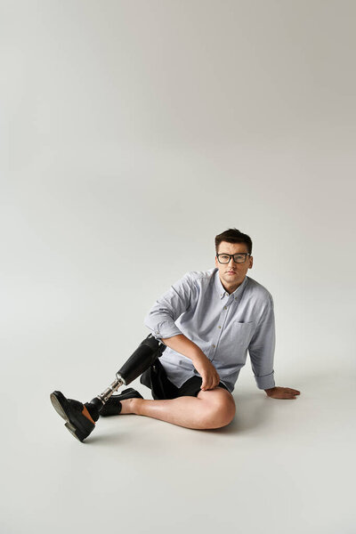 Young man relaxes on the floor, highlighting his stylish prosthetic leg in a simple background.