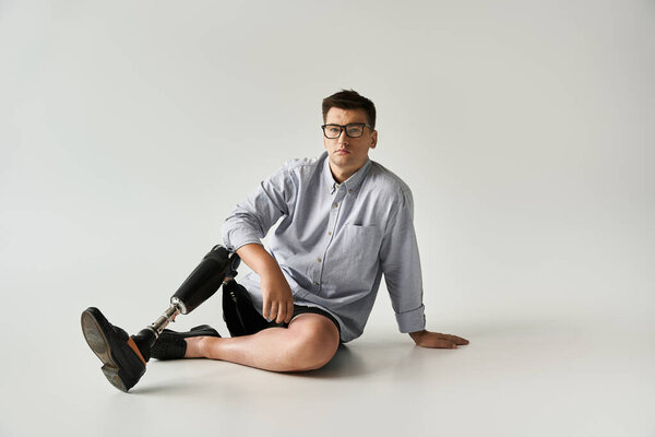 A young man sits casually on the floor, showcasing his prosthetic leg in a bright space.