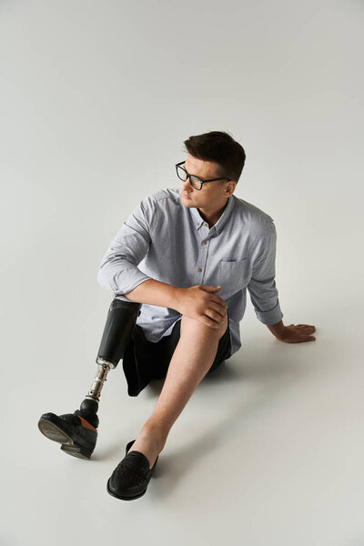 Handsome young man in casual attire sits comfortably on the floor, revealing his prosthetic leg.