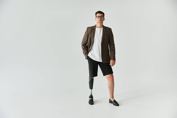 Красивый молодой человек стоит в стильной одежде и с гордостью демонстрирует свою протезную ногу..