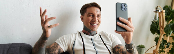 Handsome young man with tattoos smiles while chatting on his smartphone in a relaxed environment.