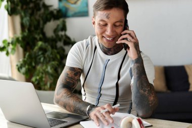 Dövmeli yakışıklı genç adam yazarken neşeli bir telefon görüşmesi yapıyor..