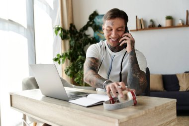 Dövmeli genç adam ofisteki bir masada otururken telefonla konuşuyor..