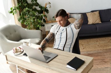 Masasında oturan yakışıklı genç adam, rahat bir iç mekanda dizüstü bilgisayarına odaklanmış..