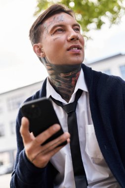 Dövmeli yakışıklı genç adam günışığının tadını çıkarırken telefonunu kullanıyor..