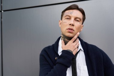 Dövmeleri olan genç yakışıklı bir adam şık duruyor, şehir ortamında kendine güveni var..