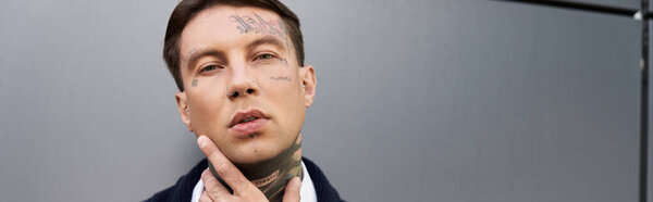 Handsome young man with tattoos poses thoughtfully against a modern gray background
