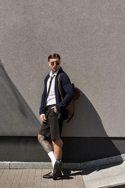 Genç adam moda kıyafetler ve güneş gözlüğü takarken dövmelerini sergiliyor..