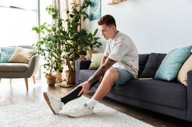 Adam kanepede oturup, rahat bir atmosferi kucaklarken protez bacağını düzeltiyor..