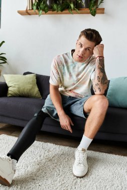 Genç yakışıklı bir adam kanepede oturup protez bacağını göstererek kendine güvenini ve tarzını sergiliyor..