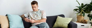 Genç bir adam kanepede rahat rahat akıllı telefonunu kullanıyor..