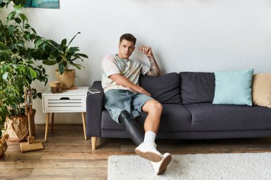 Protez bacağı olan genç bir adam yeşil bir kanepenin üzerinde rahatlar..