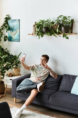 A handsome young man with a prosthetic leg smiles and poses while taking a selfie at home. clipart