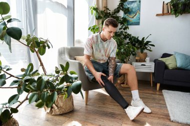 Genç ve yakışıklı bir adam modern bir sandalyede oturur, protez bacağını ev bitkilerinin arasına yerleştirir..