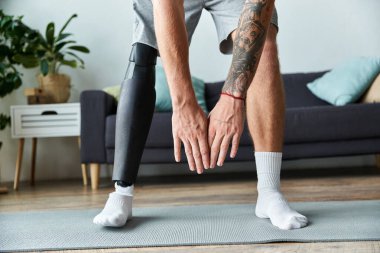 Protez bacaklı genç bir adam oturma odasında yoga yapıyor..