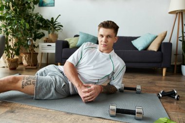 Yakışıklı genç adam yoga minderinin üzerinde yatıyor, spor kıyafetleriyle çevrili..
