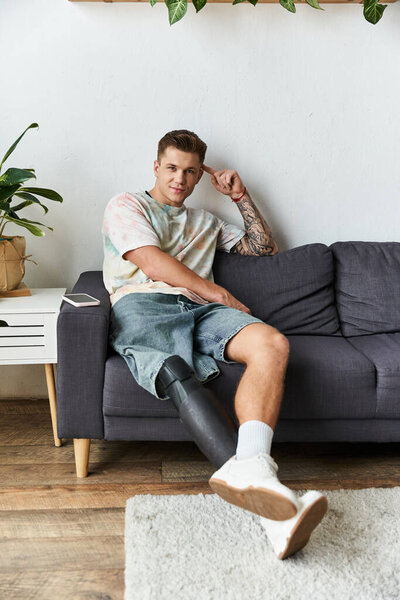 Молодой человек с протезной ногой удобно сидит на диване, наслаждаясь моментом расслабления..