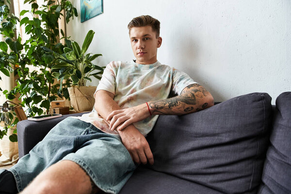 Красивый молодой человек с протезной ногой наслаждается отдыхом на диване в окружении зелени.