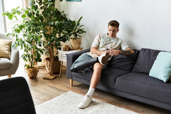 Молодой человек на диване использует свой смартфон, регулируя протез ноги..