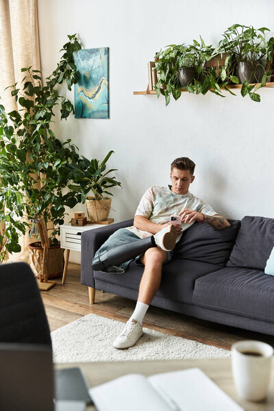 Красивый молодой человек удобно сидит на диване, занимаясь с телефоном в стильной гостиной.