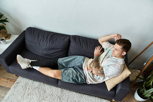 Молодой человек расслабляется на стильном диване, гордо показывая свою протезную ногу.