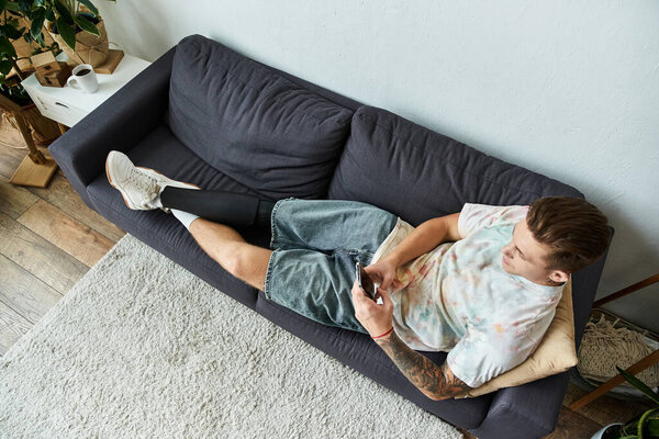 Красивый молодой человек удобно сидит на диване, общаясь со своим смартфоном..