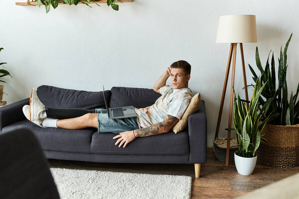 Молодой красивый мужчина с протезной ногой лежит на диване, сосредоточенный на ноутбуке..