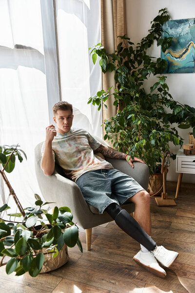 Молодой человек сидит удобно в кресле, демонстрируя свою протезную ногу в ярком, уютном пространстве..
