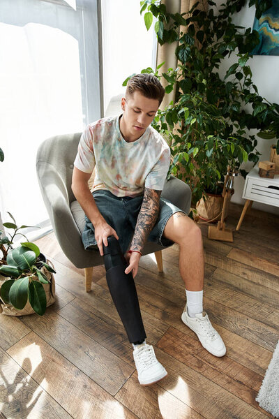 Красивый молодой человек сидит в уютном кресле, регулируя свою протезную ногу в стильном помещении.