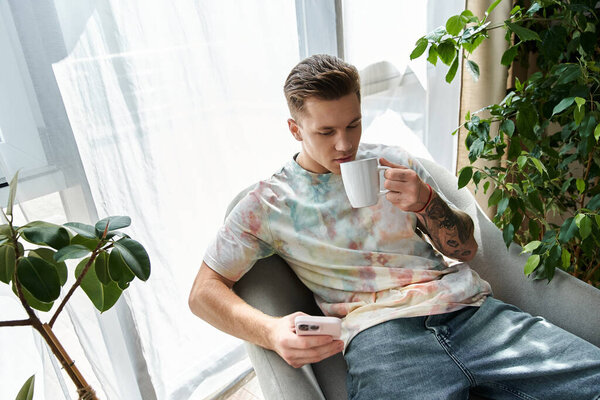 Красивый молодой человек пьет кофе, проверяя телефон в уютной комнате..