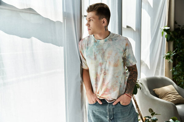 Красивый молодой человек стоит у окна, погруженный в глубокие размышления днем.