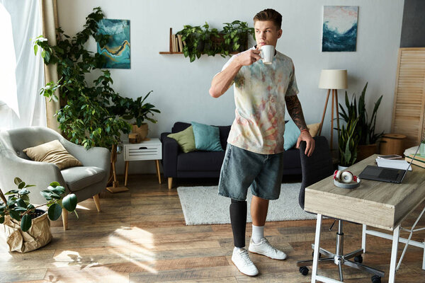 В уютной комнате молодой человек с протезной ногой наслаждается кофе, излучая уверенность.