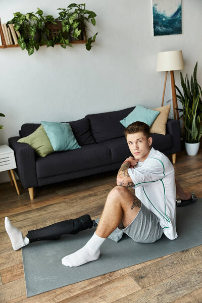 A young handsome man sits on a mat, looking thoughtful, in a modern living room filled with plants.