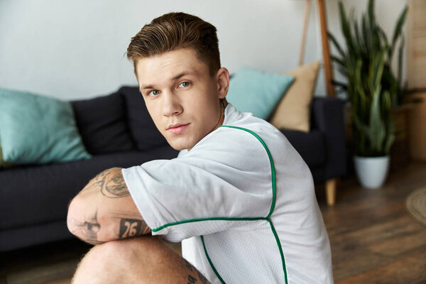 Стильный молодой человек сидит на спокойном фоне.