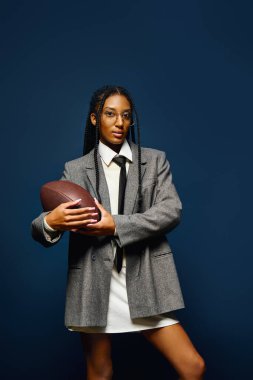 A confident young woman showcases her unique style while holding a football in her arms. clipart