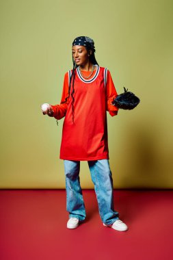 Sportif kıyafetler giymiş, elinde beyzbol topu ve eldiven tutan genç bir kadın, kendine güven ve beceri yayıyor..